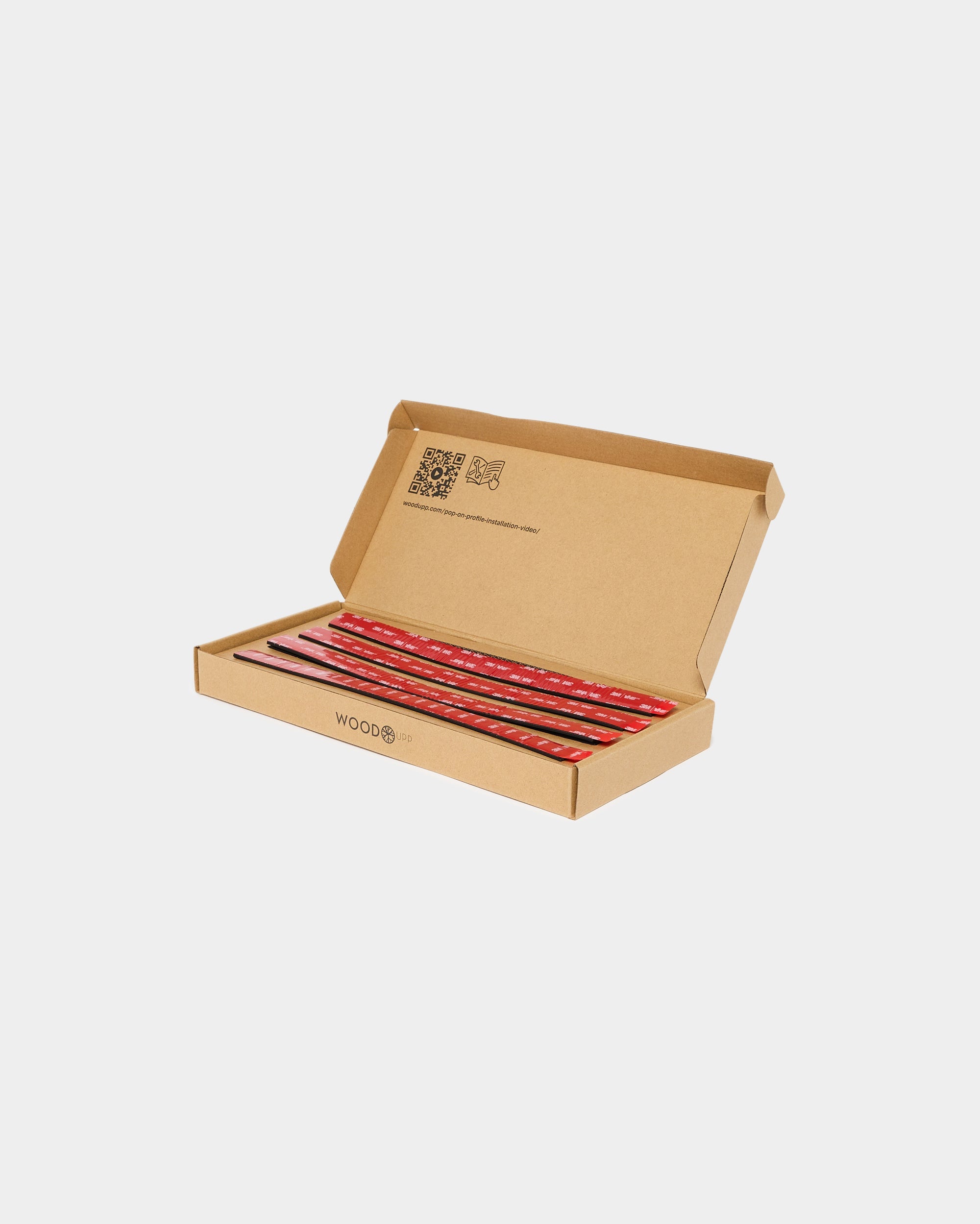 Open cardboard box with several red graphite pencils neatly arranged in a row on a white background. No WoodUpp acoustic panels or accessories visible.